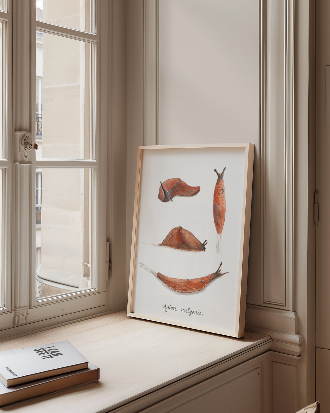 Framed artwork of slugs on a windowsill with books below